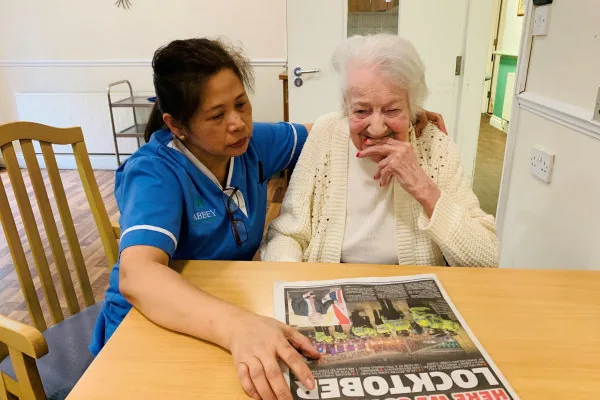 Carer reading newspaper with resident at Bridge House Care Centre, Wallington
